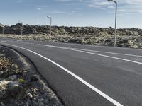 a street sign sits next to an empty roadway and rocky landscape surrounding it and some lights are on all the poles