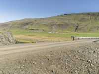 a car traveling down a dirt road near mountains and fields covered in sheep grazing on the side