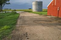 an old road passes a red barn and a red silo on the other side