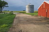 an old road passes a red barn and a red silo on the other side