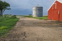 an old road passes a red barn and a red silo on the other side