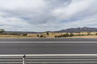 an empty street with the mountains in the background and a fenced off area on the other side