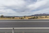 an empty street with the mountains in the background and a fenced off area on the other side