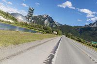 a long empty road with green trees, mountains and a building in the distance with blue sky above