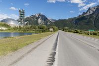 a long empty road with green trees, mountains and a building in the distance with blue sky above