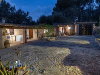 a courtyard with lights in the night and two small houses in the distance in the background