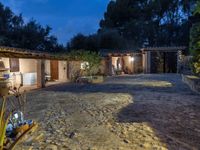 a courtyard with lights in the night and two small houses in the distance in the background