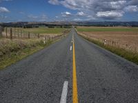 a rural road in the middle of the field with grass in the middle of it and an empty yellow line along both sides