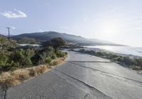 a street with gravel road and vegetation along the road near mountains by water area and mountain range