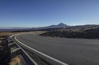 a road with a mountain in the distance near the ocean on the right side of it