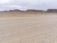 a man in a long black jacket rides a motorcycle through the desert landscape in front of mountains