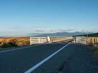 the road has two fences and some mountains in the back ground in the distance, a bridge is on the left