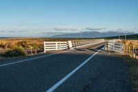 the road has two fences and some mountains in the back ground in the distance, a bridge is on the left