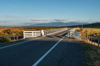 the road has two fences and some mountains in the back ground in the distance, a bridge is on the left