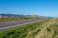 a road that has grass growing and a yellow sign by the side of it indicating which to choose if there is a direction