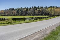 a country road with fence in the middle of it and trees to the side on both sides