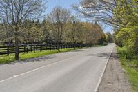 a road in front of some trees by a fence on a sunny day, with no traffic