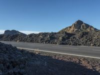 a small road that has mountains and rock in the back ground with a blue sky in front of it