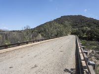 a view from a bridge overlooking trees and a mountain range of hills behind a bridge