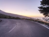 a road and mountain at sunset with a person on the side taking a photo of it