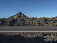 a road that is next to the rocks and a mountain in the distance with a car parked on it