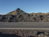 a road that is next to the rocks and a mountain in the distance with a car parked on it