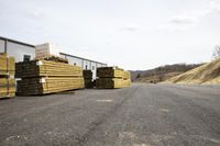 wood beams stacked on top of each other on a gravel road near a warehouse building