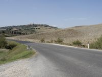 an empty road that goes to the town of roubroures, with hills and bushes in the distance