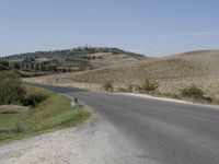 an empty road that goes to the town of roubroures, with hills and bushes in the distance