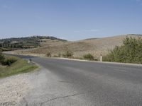 an empty road that goes to the town of roubroures, with hills and bushes in the distance