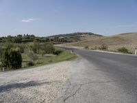 an empty road that goes to the town of roubroures, with hills and bushes in the distance