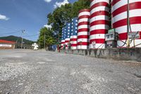 several patriotic metal tanks with american flag decorations in the background of a road lined with gravel