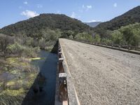 a view from a bridge overlooking trees and a mountain range of hills behind a bridge