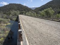 a view from a bridge overlooking trees and a mountain range of hills behind a bridge