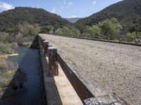 a view from a bridge overlooking trees and a mountain range of hills behind a bridge