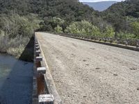 a view from a bridge overlooking trees and a mountain range of hills behind a bridge