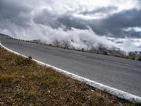 a person riding on a road with a motorcycle in the background as clouds travel through the mountains