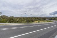 the view of the roadway looking over trees and hill tops in the distance, with a small white car on the road and cars on it