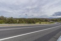 the view of the roadway looking over trees and hill tops in the distance, with a small white car on the road and cars on it