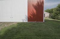 the horse is grazing in the field near the barn's back door, and in front of the white building