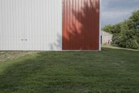 the horse is grazing in the field near the barn's back door, and in front of the white building