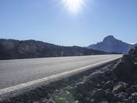 a motorcycle driving along the side of a mountain road on rocks and dirt with the sun shining