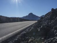 a motorcycle driving along the side of a mountain road on rocks and dirt with the sun shining