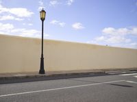 an empty street next to an empty wall and lamp post against the sky with clouds