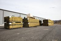 stacks of wooden lumber stacked against each other in a parking lot outdoors with the buildings in the background