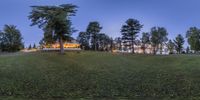 a grassy hill with a lake in the background at night and a large house at the top