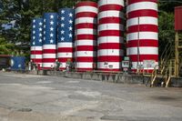 a row of cylindrical american flags near a red truck and building with a yellow truck behind it