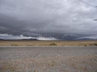 a desert with a field, and some power lines and electrical poles and dark clouds