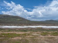 a white horse is in an empty field with the mountains in the background and a grassy area below