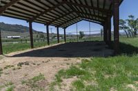 a covered area with the grass and animals standing inside of it and there are horses